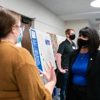 Scholar presenting poster to guest, both wearing masks.